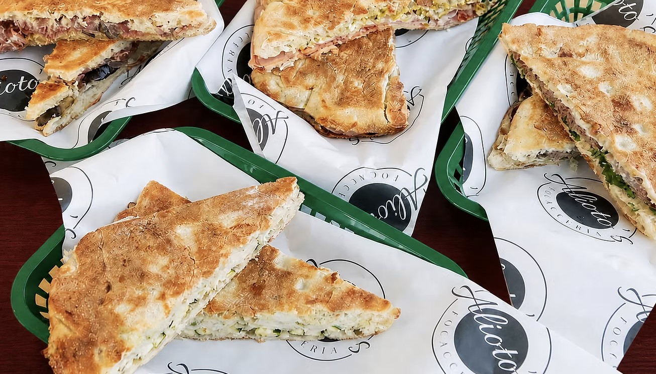 Toasted focaccia sandwiches on Alioto&rsquo;s printed paper in green baskets
