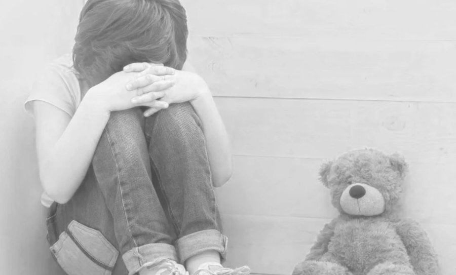 Child with head down beside a teddy bear