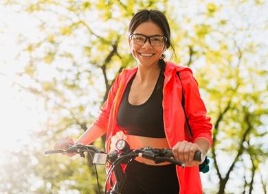Smiling woman in a coral jacket holding a bike handlebar outdoors